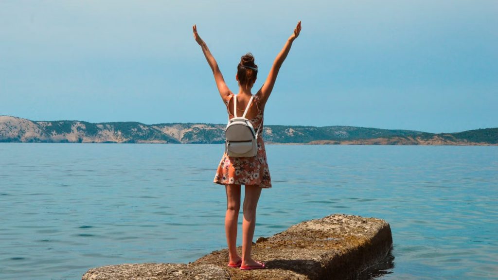 Woman in floral dress with arms raised, enjoying the view by the sea in Croatia.
