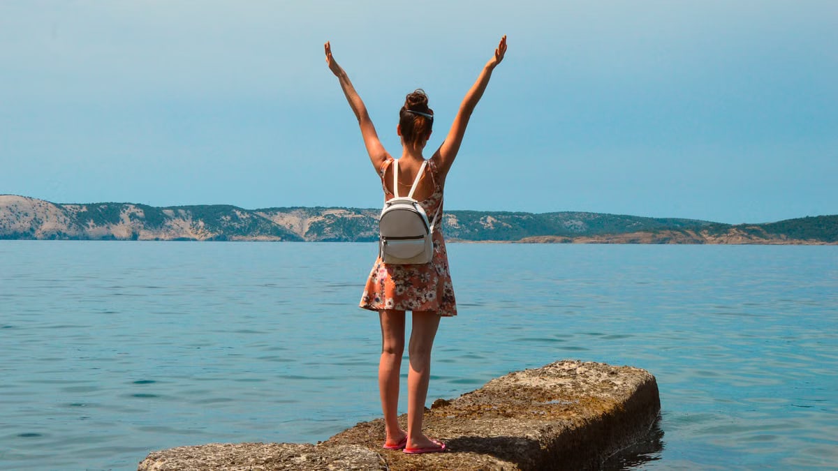 Woman in floral dress with arms raised, enjoying the view by the sea in Croatia.